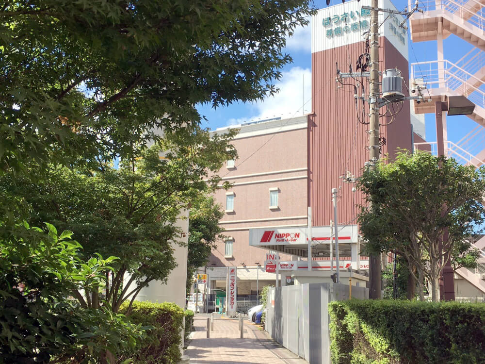 道なりに右にが曲がると日本レンタカーの営業所が見え、その奥の茶色の建物が目的地です。